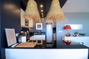 Una cocina moderna con una isla central, iluminación colgante y un refrigerador.