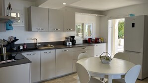 Una cocina moderna con una isla central, armarios blancos y un comedor con mesa y sillas.