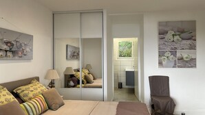 Un dormitorio con cama, lámparas de noche, armario, baño con lavabo y una silla.