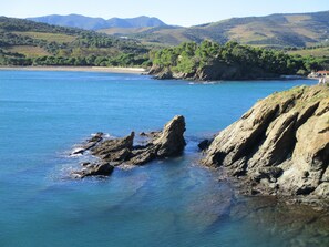 Paisaje costero con aguas azul cristalino, afloramientos rocosos y colinas distantes.