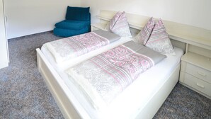 A bed with patterned bedding, a blue chair, and a bedside table with drawers. - Ferienwohnung 35m² (Kötschach-Mauthen)