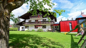 A two-story building with a balcony, a red play structure, and a well-maintained lawn. - Ferienwohnung 35m² (Kötschach-Mauthen)