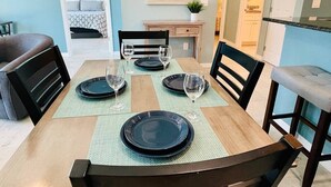 Ein Essbereich mit einem Holztisch, gedeckt für vier Personen, umgeben von Stühlen und mit Blick in ein Schlafzimmer.