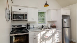 A modern kitchen with white cabinets, a stainless steel refrigerator, a microwave, an oven, and a coffee maker. - The Aspen . Trailside Lodging (Millersburg)