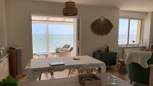 Ein geräumiges Zimmer mit großem Tisch, Stühlen, Meerblick und einer gemütlichen Sitzecke mit Sessel und kleinem Tisch.