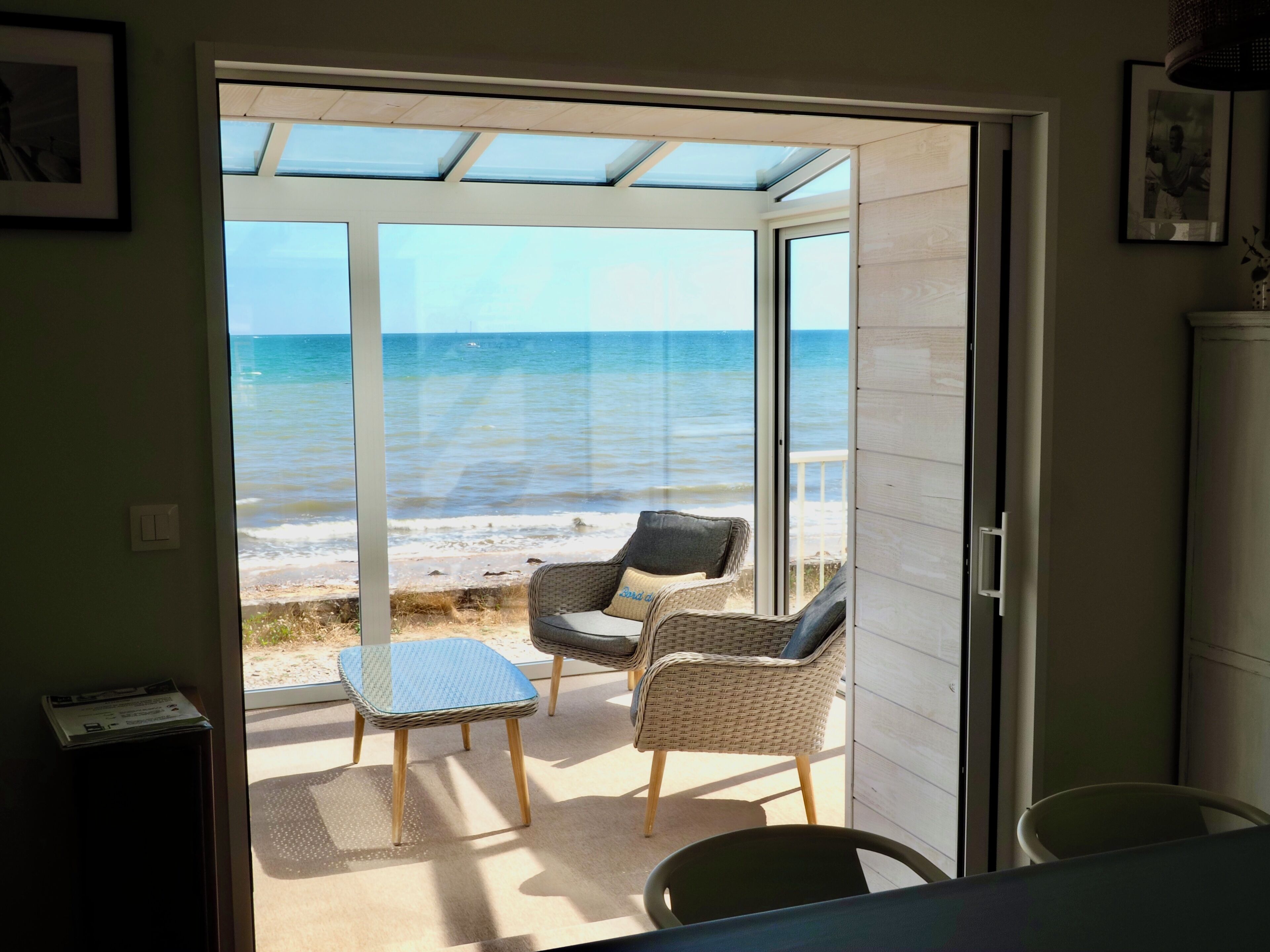 Una habitación con puerta de vidrio que da a vista de playa, mobiliario de mimbre y una pequeña mesa.