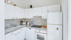Moderni keittiö, jossa on valkoiset kaapit, sisäänrakennettu astianpesukone, jääkaappi ja kahvinkeitin.