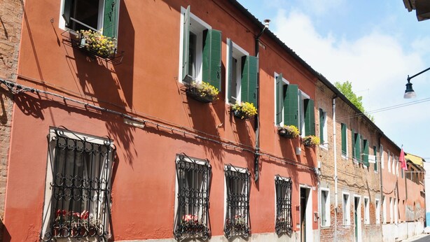 A row of red and white buildings with green shutters and flower boxes.