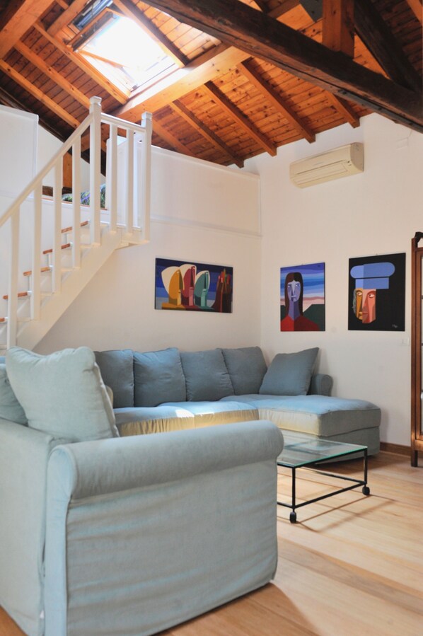 A living room with a light blue sofa, a glass coffee table, and a wooden staircase. There are abstract paintings on the wall. - Spacious two-bedroom, two-bathroom apartment in old town, Biennale area (Venezia)