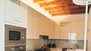 A kitchen with white cabinets, a wooden ceiling, a built-in oven, a microwave, a sink, and a fan.