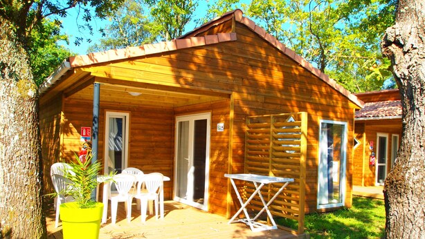 A wooden cabin with a porch, a table, and chairs.