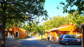 A row of wooden cabins with gravel driveways, outdoor seating, and a parked car.