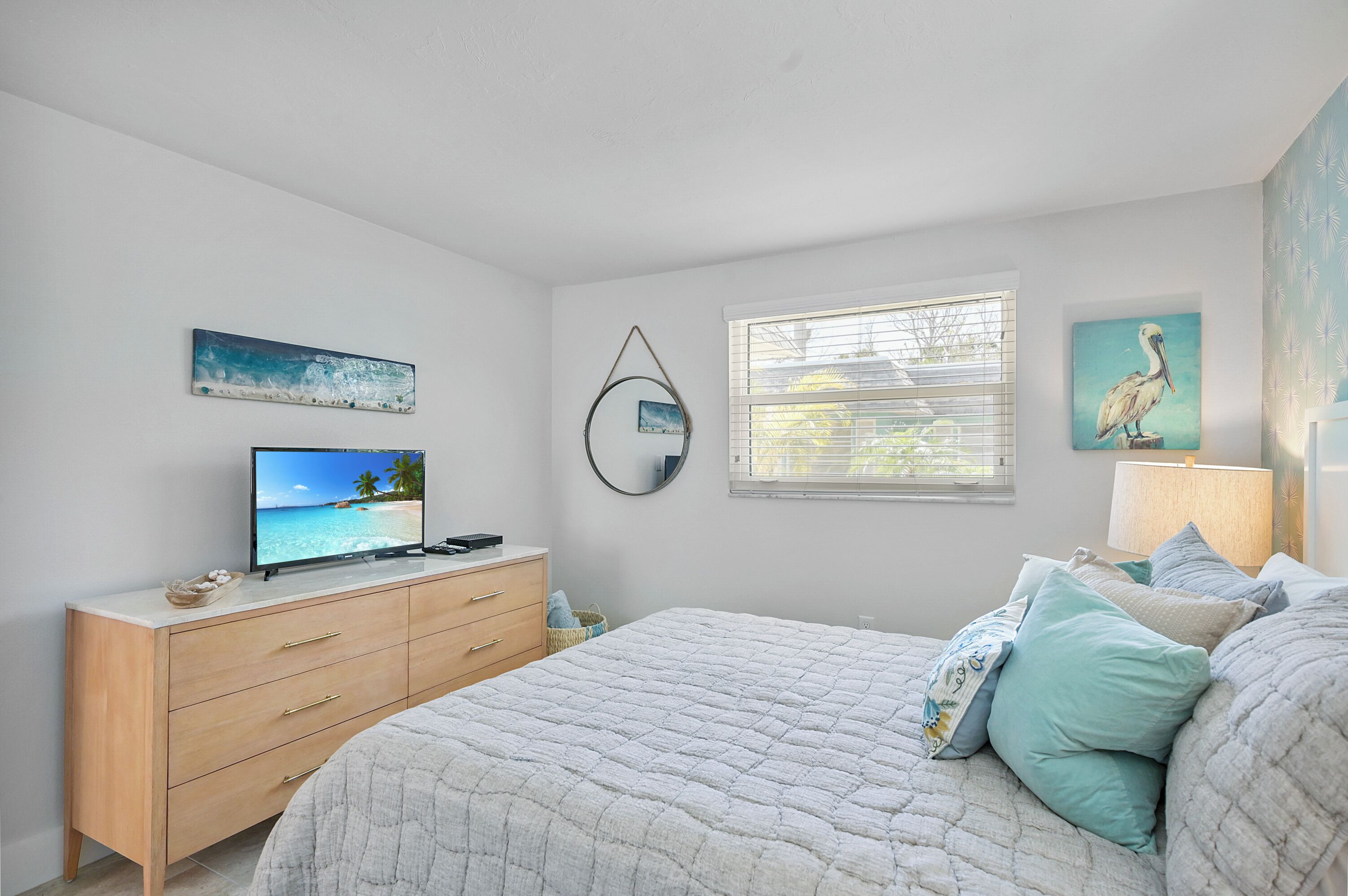 A bedroom with a bed, a dresser, a TV on the dresser, a window, and wall art.
