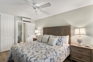 A bedroom with a large bed, a wooden headboard, two bedside tables with lamps, and a ceiling fan. - Updated Kamaole Sands Condo (Kihei)