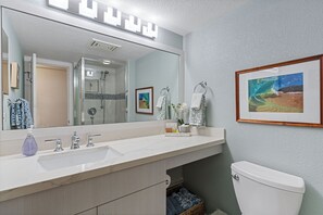A bathroom with a large mirror, two sinks, a toilet, and a framed picture on the wall. - Updated Kamaole Sands Condo (Kihei)