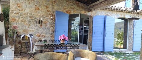 A stone-walled patio with a table and chairs, a potted plant, and blue shutters.