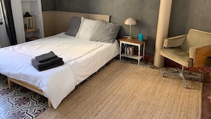A neatly made bed with a white duvet and folded towels, a bedside table with a lamp, a chair, and a patterned rug on a tiled floor. - House with garden downtown (Sète)