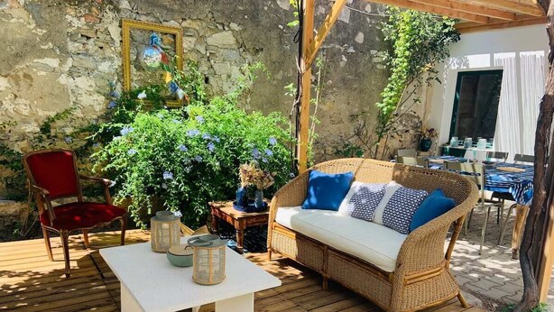 A wooden deck with a wicker sofa, a red chair, and a white table with decorative items. - House with garden downtown (Sète)
