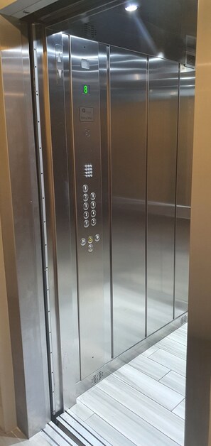 Ein Fahrgastaufzug mit Metallverkleidung, einem digitalen Display für die Zahl 8 und einer Bedienkonsole mit Knöpfen.