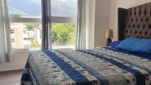 A bedroom with a large bed, a tufted headboard, and a view of buildings and trees through a window. - Exclusive Apartment Arboleda 186 (San Pedro Sula)