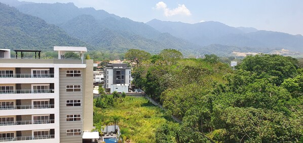 Un hotel de varios pisos con balcones y zona de piscina, rodeado de vegetación exuberante y montañas al fondo.