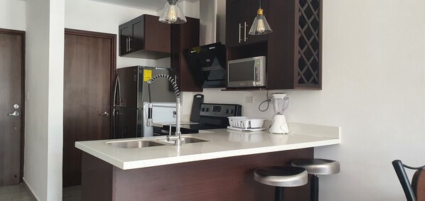 Una cocina moderna con armarios de madera oscura, electrodomésticos de acero inoxidable, encimera blanca y dos taburetes de bar.
