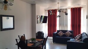 A living room with a sofa, a dining table with chairs, a TV, and a red curtain. - Exclusive Apartment Arboleda 186 (San Pedro Sula)