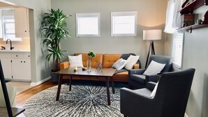A living room with a sofa, armchair, coffee table, and a large plant.