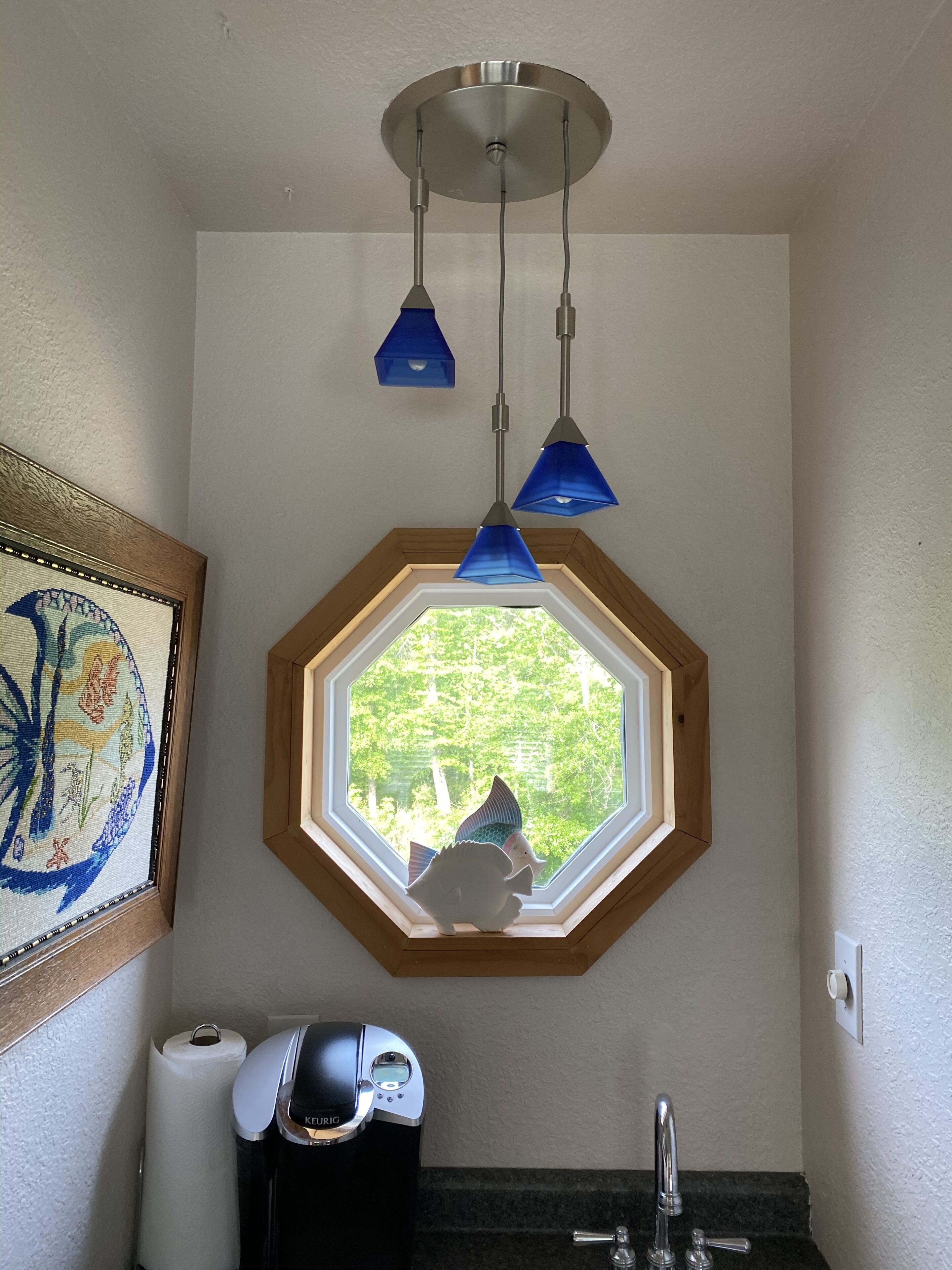 A bathroom with a skylight, a framed artwork, a coffee maker, and a sink.
