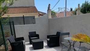 Un espace patio extérieur doté d’un sol en pierre, de meubles en osier noir et d’une petite table ronde agrémentée d’une plante jaune.