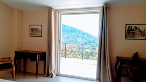 A room with a large sliding glass door leading to a balcony with a mountain view. There are two framed artworks on the walls and a wooden desk with a chair. - VERY NICE VILLA WITH HEATED POOL AND SUPERB VIEW ON BARGEMON AND HILLS (BARGEMON)