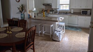 Una cocina moderna con armarios blancos, una isla central y un comedor con mesa y sillas de madera.