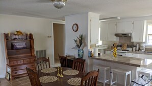Un comedor con una mesa y sillas de madera, un reloj en la pared y una cocina al fondo.