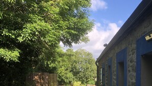 A stone building with blue window frames, a grassy yard, and a large tree. - Je Recharge mes "batteries" à Sainte Marine (Combrit)