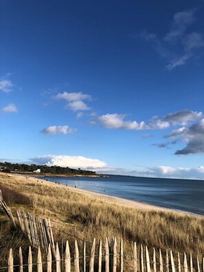 Una platja amb una tanca de fusta al primer terme, un cel blau clar i un mar tranquil.