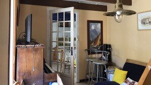A room with a piano, a wooden cabinet, a door leading to another room, a metal chair, a bed with pillows, and a ceiling fan. - Je Recharge mes "batteries" à Sainte Marine (Combrit)