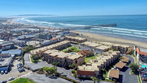 Vista aérea de una zona residencial costera con playa, un muelle y un conjunto de edificios de apartamentos.