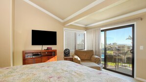 Habitación de hotel con cama, televisión, escritorio con ordenador, silla y puerta corrediza de vidrio que da a un balcón con vistas a la ciudad.