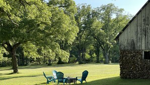 A grassy outdoor area with a stone wall, a wooden barn, and green Adirondack chairs. - Countryside paradise 6 miles to Stockton Lake! We now have high-speed internet! (Stockton)