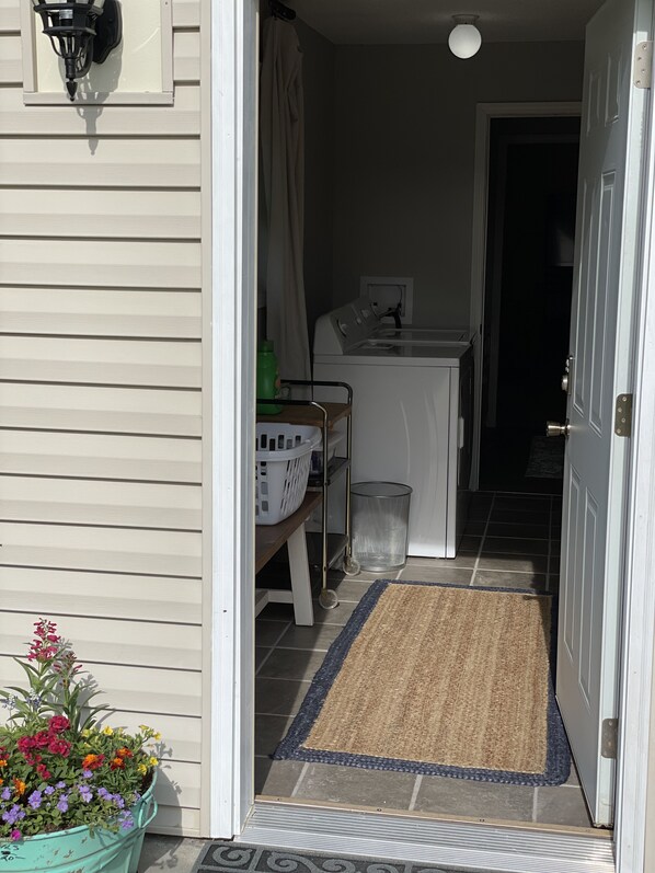 A narrow entryway with a door, a small table with a basket, a washing machine, and a potted plant with flowers.