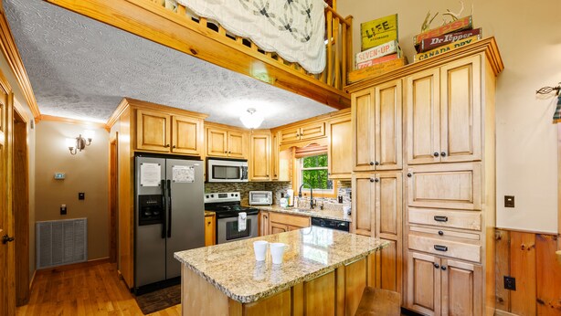 A kitchen with wooden cabinets, a granite countertop, stainless steel appliances, and a small island with stools. - Beautiful Amazing Setting, Fire Pit & Pool Table, Large Wrap Around Deck w/ Spa! (Sevierville)