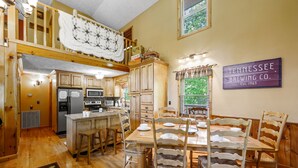 A spacious kitchen with wooden cabinets, a dining area with a wooden table and chairs, and a sign for Tennessee Brewing Co. on the wall. - Beautiful Amazing Setting, Fire Pit & Pool Table, Large Wrap Around Deck w/ Spa! (Sevierville)
