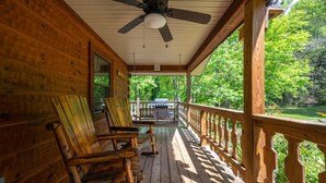 A wooden porch with rocking chairs, a ceiling fan, and a view of a green landscape. - Beautiful Amazing Setting, Fire Pit & Pool Table, Large Wrap Around Deck w/ Spa! (Sevierville)