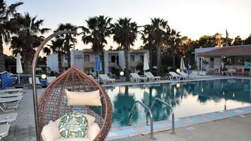 A pool area with lounge chairs, a hanging chair, and a building labeled 'PARTMENTS LYMPIA' in the background.