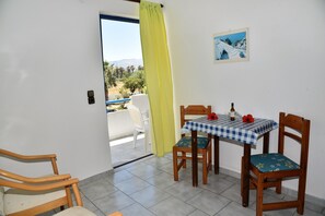A balcony with a table and chairs, a view of the outdoors, and a door with a curtain. - 1-bedroom Kos Olympia Apartment at Lambi Beach (Kos)