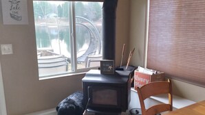 A cozy room with a wood-burning stove, a window overlooking a lake, and a dining table with chairs. - Bluegill lake -Lake front retreat (Harrison)