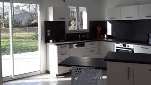 Una cocina moderna con armarios blancos, encimera negra y una puerta corredera de vidrio que da a un jardín.