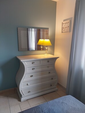 A room with a white dresser, a mirror with a geometric frame, and a yellow lamp.