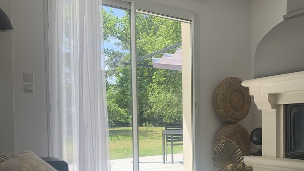Una sala de estar moderna con un sofá, una mesa y una chimenea. Hay una puerta corrediza de vidrio que da a un patio con muebles de exterior.