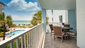 A balcony with a view of a pool and beach, furnished with wicker chairs and a table. - Beachfront 3BR Condo with Oversized Gulf View Balcony, Pool and Spa (Indian Shores)